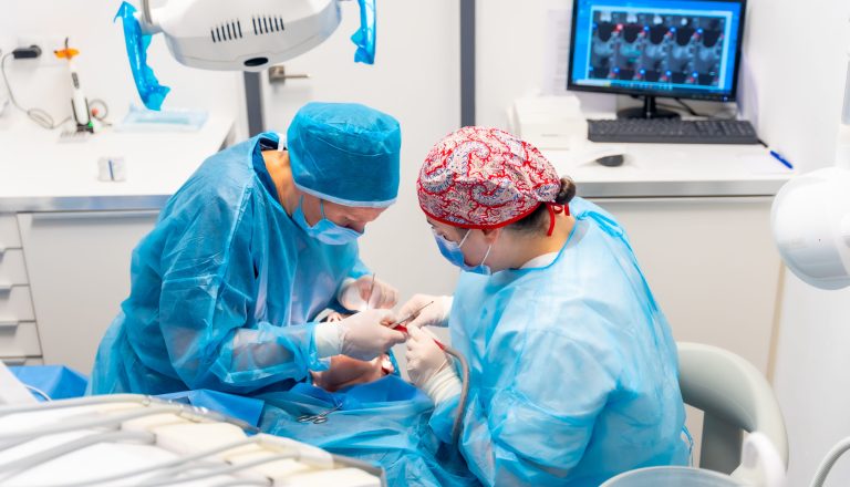 Female dentists in blue scrubs performing a complicated operation on a female patient, sucking blood